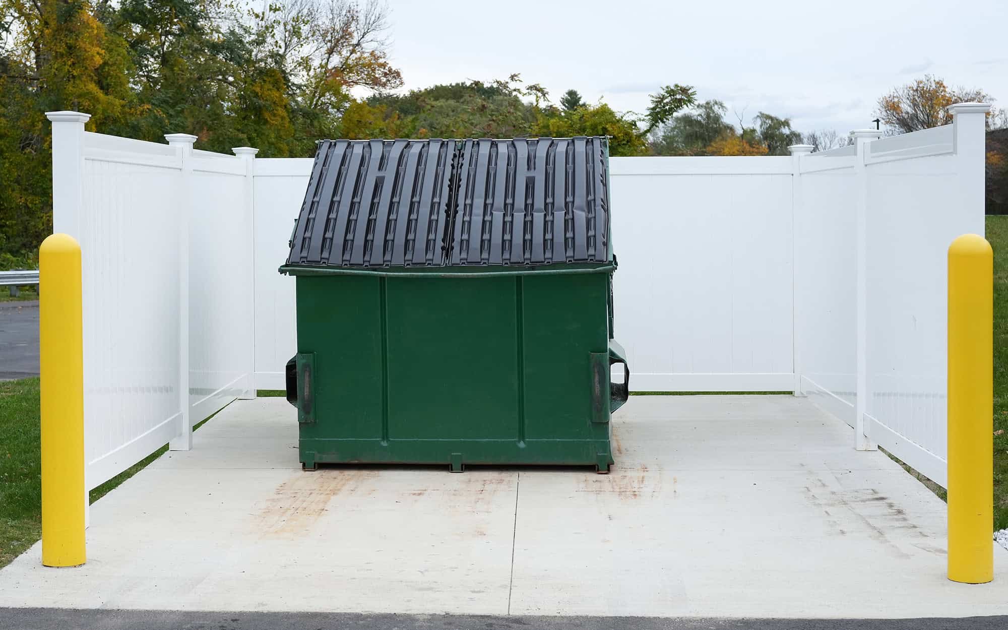 Dumpster with white fencing on a dumpster pad