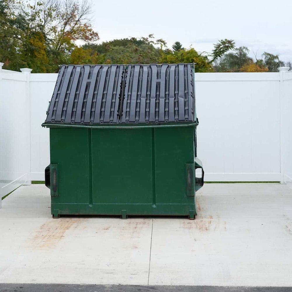 Dumpster with white fencing on a dumpster pad